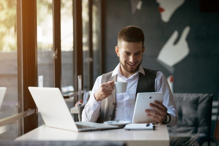 man working in a cafe looking at tablet device