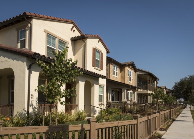 A row of new homes with fenced yards along a sidewalk