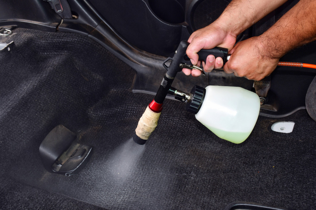 A person spraying a cleaning solution on a car's floor